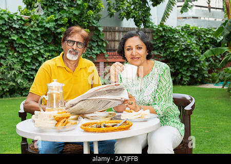 Vieux couple Man reading newspaper et femme à boire le thé au petit-déjeuner-en-cour de leur maison à Banque D'Images