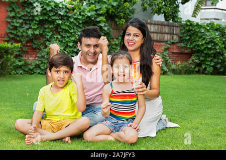 Happy-Family Parents et deux enfants Fils Fille assis-sur-grass et de poings-part gagner succès Célébration en-jardin Banque D'Images