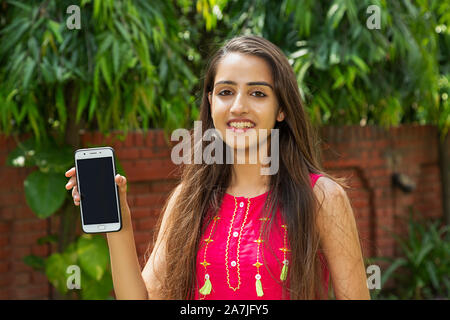 Happy young woman showing Téléphone cellulaire avec écran vide en-dehors jardin Banque D'Images