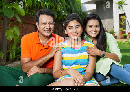 Père et mère de famille heureuse avec adolescent fille assise sur l'herbe et se détendre dans la cour de leur maison Banque D'Images