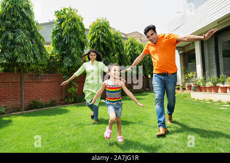 Heureux les jeunes Indiens et les parents de famille petite fille courir ensemble en face de leur maison dans le jardin Banque D'Images