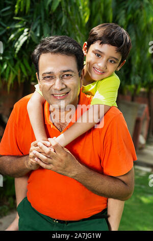 Portrait de petit fils bénéficiant piggyback ride sur son père en arrière-jardin extérieur Banque D'Images