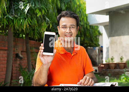 Smiling Young man Showing Smart Phone avec écran vide en-cour près de leur maison Banque D'Images