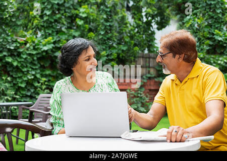 Les Indiens Happy Senior couple homme et femme à l'aide d'ordinateur portable et avec du papier journal dans la cour de leur chambre le matin d'été Banque D'Images