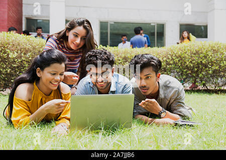 Quatre garçons et filles collège étudiants amis-couché sur l'Herbe-Looking-At In-Outside-écran de l'ordinateur portable étudiant Campus Banque D'Images