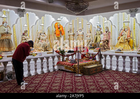 Un homme d'âge moyen anonyme bows, prie et médite devant les statues de divinités hindoues au Satya Narayan Mandir à Queens, New York. Banque D'Images