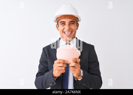 Architecte beau man wearing helmet holding piggy bank sur fond blanc isolé avec un visage heureux et souriant debout avec un sourire confiant Banque D'Images