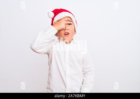 Bel enfant boy wearing Santa hat Noël isolé debout sur fond blanc avec des pics de shock couvrant le visage et les yeux avec la main, à throu Banque D'Images