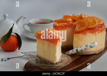 Vue frontale d'un morceau d'orange confite gâteau avec le reste du gâteau, une orange fraîche, une théière et une tasse de thé en soft-focus à l'arrière-plan Banque D'Images