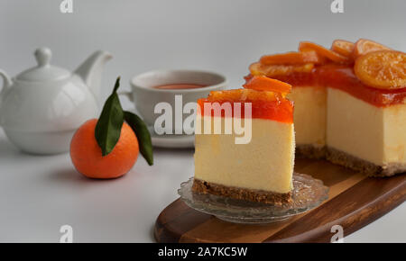 Vue frontale d'un morceau d'orange confite gâteau avec le reste du gâteau, une orange fraîche, une théière et une tasse de thé en soft-focus à l'arrière-plan Banque D'Images