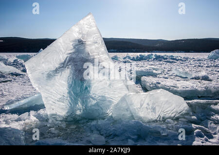 Un énorme morceau de glace dans le lac Baïkal gelé, derrière laquelle se tient un homme. Un ciel clair, les collines derrière un lac avec de la neige et glace dispersés. Banque D'Images