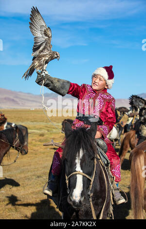 Jeune garçon mongol mongol traditionnel en tenant sa robe de pèlerin à cheval. Les jeunes enfants commencent l'entraînement avec les faucons avant de travailler avec g Banque D'Images