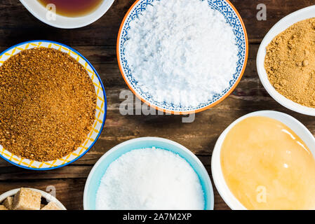 Différents types de Sucre et édulcorants dans les bols, tels que noix de coco, canne à sucre pur, le glaçage, le sirop d'érable, sucre mou brun foncé, miel, cubes démérara Banque D'Images