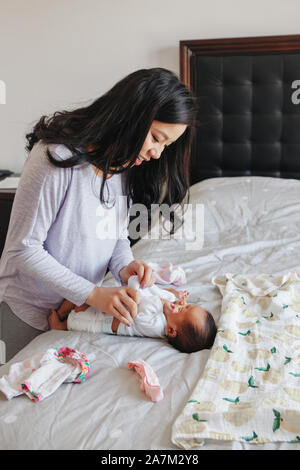 Asiatique chinois mère occupé l'évolution des vêtements pour bébé nouveau-né bébé fille. Accueil Vie familiale naturelle et authentique moment matin rou Banque D'Images