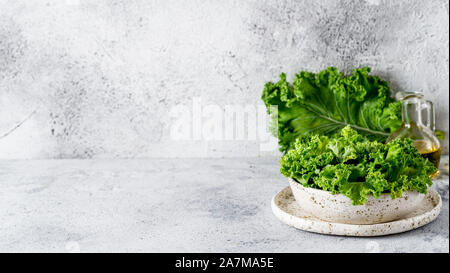 Feuilles de chou vert en blanc craft bol sur fond de ciment gris. La saine alimentation, la nourriture végétarienne, régimes concept. Copie espace gauche. Avantages santé kale. Banner Banque D'Images