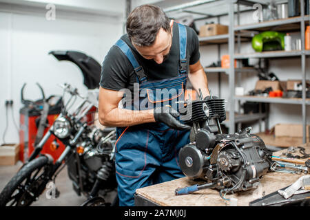 Workman en salopette démontage moteur moto lors d'une réparation à la table de travail de l'atelier Banque D'Images