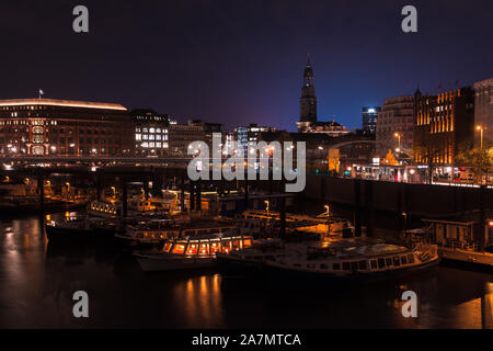 Hambourg, Allemagne - le 29 novembre 2018 : nuit vue sur la rue de la ville de Hambourg avec ses bateaux amarrés dans le vieux port et l'église Saint Michel sur un arrière-plan Banque D'Images