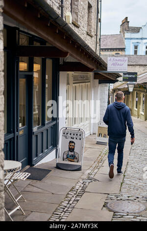 Homme passant devant un magasin de barbiers dans une rue ancienne et étroite de petits magasins indépendants à Kendal, Cumbria, Royaume-Uni, en bordure du Lake District Banque D'Images