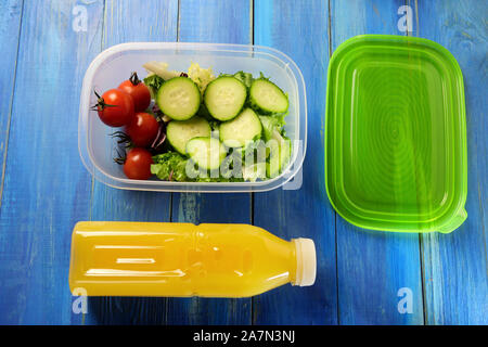Lunch Box en plastique avec salade de concombre frais et tomates cerises sur table en bois bleu. A proximité, bouteille de jus d'orange et capuchon vert. En bonne santé Banque D'Images