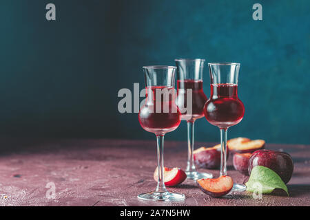 Les prunes strong boisson alcoolisée dans grappas wineglass de rosée. Alcools, slivovica, de prunes ou de prunes prunes mûres avec de la vodka sur le bleu foncé et bordeaux Banque D'Images