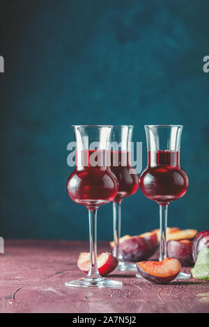 Les prunes strong boisson alcoolisée dans grappas wineglass de rosée. Alcools, slivovica, de prunes ou de prunes prunes mûres avec de la vodka sur le bleu foncé et bordeaux Banque D'Images