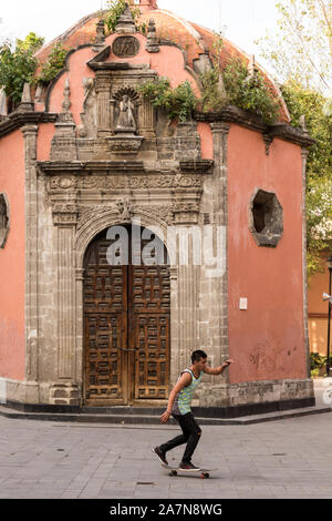 Un jeune garçon sur un skateboard passe la toute petite chapelle de style baroque de la Concepción Cuepopan savent aussi que le La Conchita ou la Chapelle des morts dans la Concepcion carré de la ville de Mexico, Mexique. Banque D'Images