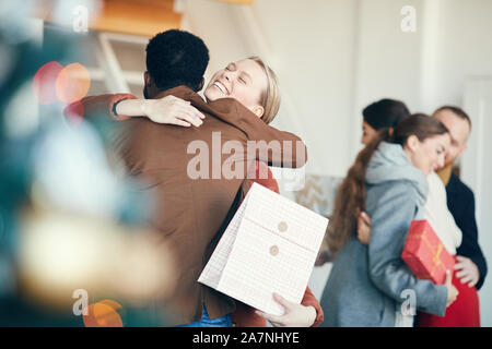 Groupe de jeunes gens modernes, l'échange de cadeaux lors d'une fête de Noël, l'accent sur smiling woman hugging ami en premier plan, copy space Banque D'Images