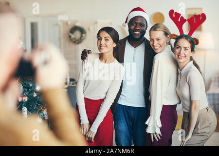 Multi-ethnic group of friends posing pour photographier pendant une fête de Noël, tous les wearing Santa hats et costumes, copy space Banque D'Images