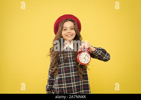 En mettant son réveil. Happy little girl holding réveil sur fond jaune. Petit enfant souriant avec horloge mécanique. Réveil Le réveil. Banque D'Images