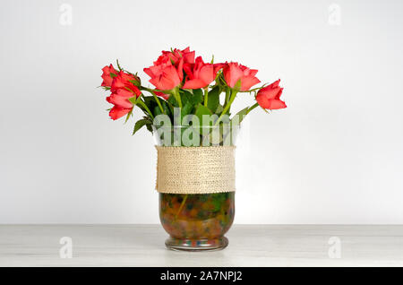 Close-up of red roses dans un vase transparent assis sur un mobilier blanc contre un fond blanc Banque D'Images