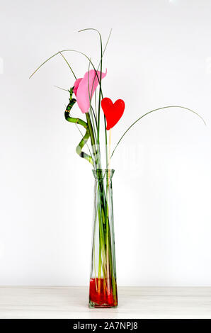 Close-up of bouquet de fleurs artificielles avec cœur rouge, branches vertes de Bambu et coloré rose calla lily dans un vase transparent sur les meubles blancs Banque D'Images