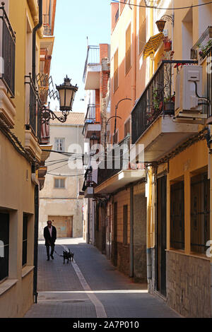 Un homme promène son chien le long d'une rue étroite et calme à Orihuela, Alicante Province, Spain. Les bâtiments offrent l'ombre qui garde la rue cool Banque D'Images