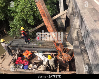 Équipe de travailleurs tirez des colonnes de béton hors de l'eau sur le fer avec ponton grue. La reconstruction de la côte du fleuve, Thaïlande Banque D'Images