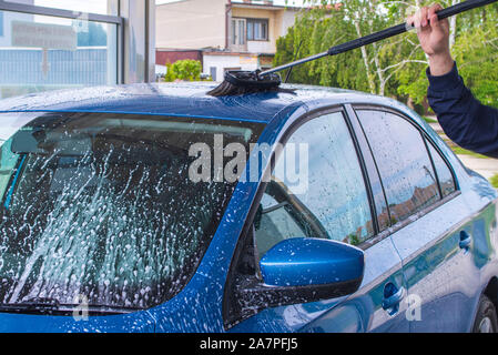 En utilisant une brosse pour laver une voiture sur une installation de lavage de voiture sur journée ensoleillée.lave-auto manuel avec de l'eau sous pression en lavage de voiture à l'extérieur.bleu manuel voiture Banque D'Images