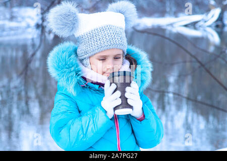 Petite fille à l'extérieur en hiver à partir d'un plateau/bouilloire mug.portrait d'une fille mignonne avec une tasse de thé chaud à l'extérieur.saison d'hiver. Banque D'Images