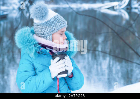 Petite fille à l'extérieur en hiver à partir d'un plateau/bouilloire mug.portrait d'une fille mignonne avec une tasse de thé chaud à l'extérieur.saison d'hiver. Banque D'Images