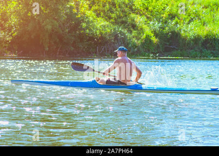 Man paddling kayak bleu et jaune sur la rivière près de la rive. Kayak concept.Un homme nage dans un canot sur la rivière. Un homme dans un bateau sous le soleil Banque D'Images