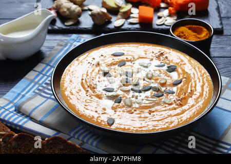 Close-up de soupe au potiron rôti crème dans un bol noir sur une table de bois, les ingrédients à l'arrière-plan sur une liste de sélection, vertical Vue de dessus Banque D'Images