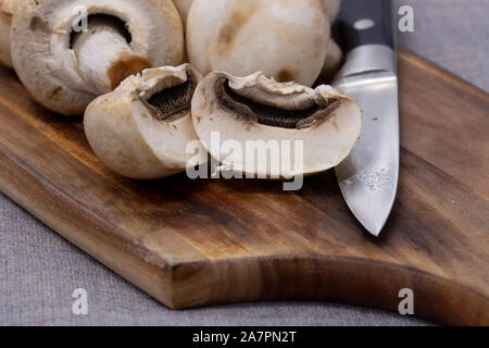 Coupe fermée champignons blancs sur une planche à découper en bois. Sur une nappe gris Banque D'Images