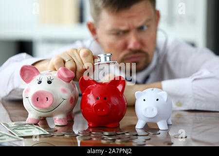 Funny businessman écouter trois piggybanks pour de l'argent Banque D'Images