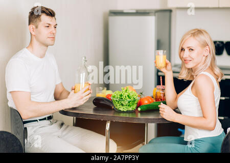 Young attractive couple having breakfast détendue assis à table de cuisine, bénéficiant d'aliments biologiques frais ensemble, à la maison, smiling at camera. Il Banque D'Images