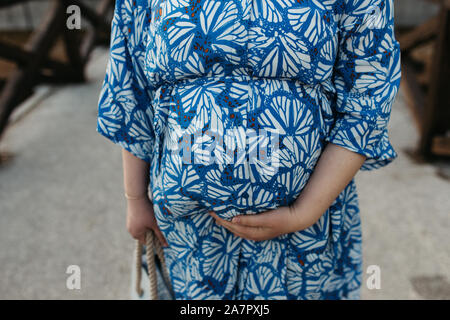 Magnifique Portrait de femme enceinte. Elle est debout au milieu de la rue et tenir la main sur son ventre. Banque D'Images