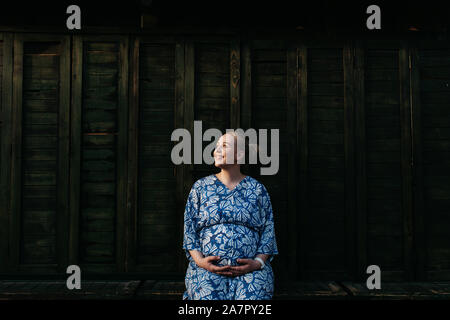 Magnifique Portrait de femme enceinte. Elle est debout au milieu de la rue et tenir la main sur son ventre. Banque D'Images