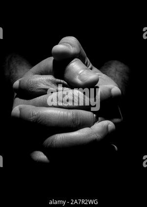 Blanc Noir un gros plan d'une mans mains jointes dans des conditions de faible éclairage clés Banque D'Images