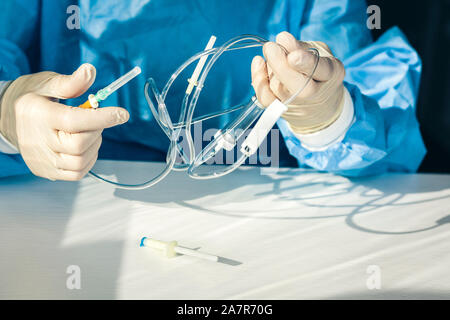 Médecin dans une blouse de chirurgien bleu et le masque tient dans sa main un système de compte-gouttes médical (antécédents médicaux avec un intraveineux est) Banque D'Images