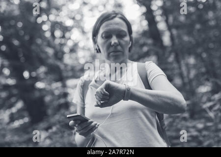 Female hiker remise en forme contrôle et synchronisation des données bracelet tracker à smartphone, image en noir et blanc, image sélective Banque D'Images