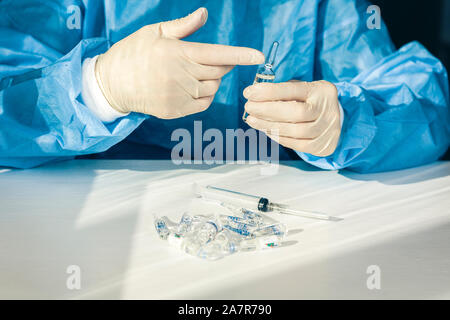Médecin dans une blouse de chirurgien bleu et le masque tient dans sa main une seringue médicale et une bouteille avec de l'insuline pour le diabète. De nombreux médicaments pour injection sur ta blanche Banque D'Images