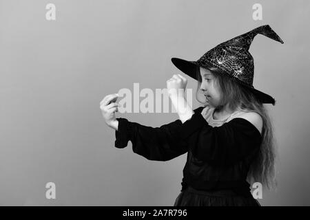 En Chapeau de sorcière pour enfants, robe et concentré face. Fille essaie de sort, isolé sur fond vert. Enfant en costume chapeau noir. Célébration de l'Halloween et concept Banque D'Images