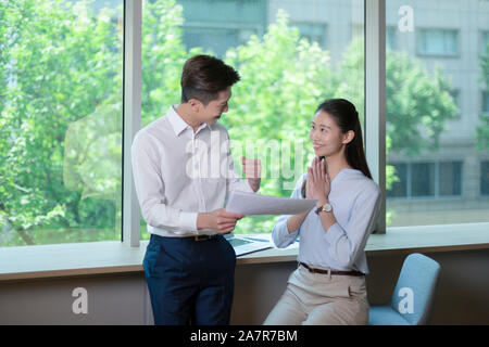 Deux happy smiling businesspeople, hommes et femmes avec des cheveux noirs et businesswear montrant les gestes de réussite dans un bureau Banque D'Images