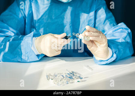 Médecin dans une blouse de chirurgien bleu et le masque tient dans sa main une seringue médicale et une bouteille avec de l'insuline pour le diabète. De nombreux médicaments pour injection sur ta blanche Banque D'Images